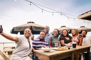Black people taking a selfie with their cell phones having a good time. African-American family enjoying a meal at a beach restaurant.
