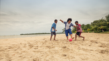 Three boys compete for the ball in a soccer game on a beach.