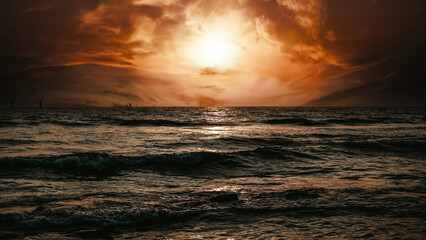 sun setting below a calm ocean horizon, golden sky, reflective water, rich clouds, slight lens...