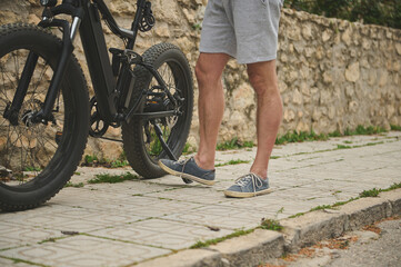 Close-up legs of a cyclist in sports shoes, pushing his bike while walking along the street. Man...