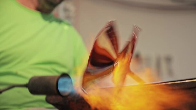 A close-up view of a glassblower's hands shaping molten glass into a delicate piece of art in Murano, Italy. Close up hand blown glass processing. Making glass in Murano Italy. 