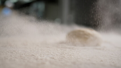 A chef sprinkles white wheat flour on a black table before preparing traditional Italian pizza. The...