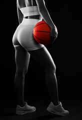 A beautiful athletic blonde girl in white shorts and a top plays basketball on a black background.