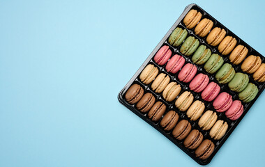 Multi-colored macarons on a blue background in a plastic box, top view