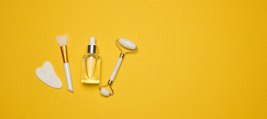 White transparent glass bottle with pipette and roller massager jade on a yellow background