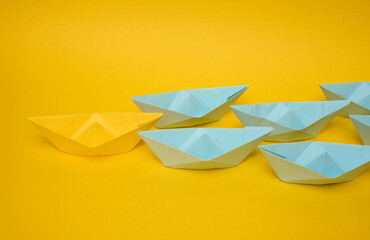Group of blue paper boats follow yellow against a yellow background. Strong leader concept, mass manipulation. Starting a business with a well-coordinated team