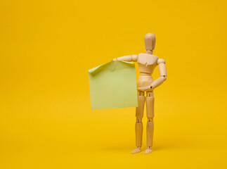 Wooden puppet puppet holding blank sticker sheet on yellow background