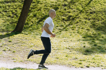 Young man running in park on sunny day. bald man runs in the park