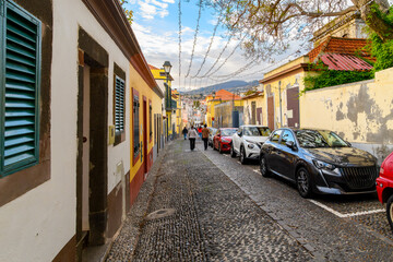 Tourists walk down the colorful Rua de Santa Maria street towards the Art of Open Doors district of shops and cafes in the Zona Velha old town of Funchal, Portugal on the Canary island of Madeira.