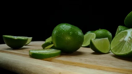 Gordijnen Close-up, a vibrant slice of fresh lime rests upon a rustic wooden cutting board, exuding freshness and vitality. The translucent membranes of the green lime slice placed on cutting board. Comestible. © Summit Art Creations