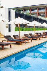 Lounge wooden sunbeds with umbrellas near swimming pool in luxury hotel for tourists to...