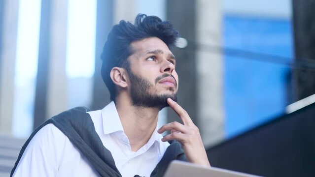 Handsome creative young man student or businessman thinks questioningly about difficult choice choose imagine plan in mind has doubts create idea at desk next to laptop at home workplace