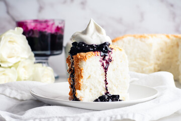 Angel Food Cake with Blueberry Sauce and Whipped Cream: Slice of sponge cake topped with dripping blueberry jam and chantilly cream on a plate