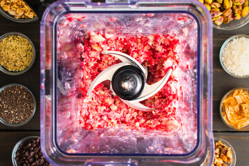 Chopped Frozen Strawberries and Bananas in a Blender: Directly above blender pitcher filled with bits of frozen fruit surrounded by smoothie toppings