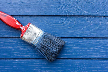 Paint brush painting blue paint onto a wooden surface