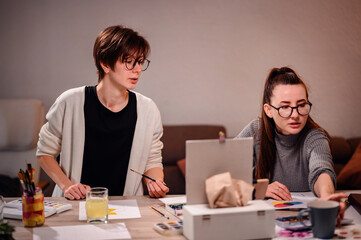 Two focused women engage in collaborative work, one sketching ideas with the other providing input, in a warmly lit office environment