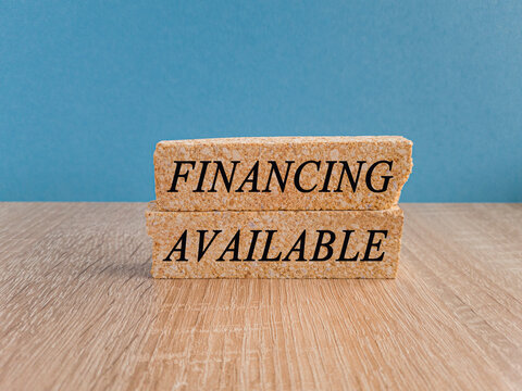Financing available symbol. Concept words Financing available on brick blocks. Beautiful wooden table, blue background. Business and financing available concept.