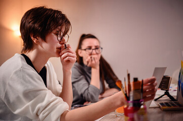 Artists captured in a moment of creation; one ponders deeply while the other paints, a scene of...