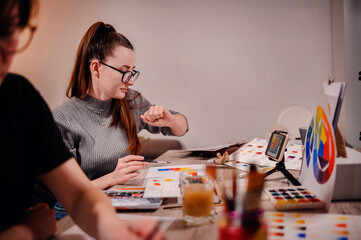 An artist meticulously studies a color chart, her gesture and intense gaze reflecting the precision...