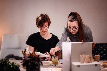 Artists share a moment of collaboration, one meticulously mixing paint while the other evaluates...