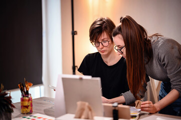 Artists share a moment of collaboration, one meticulously mixing paint while the other evaluates...