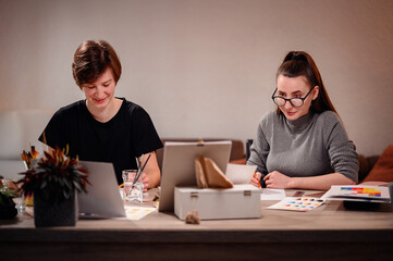 A candid shot of two artists at work, one smiling at her creation while the other is engrossed in detail, capturing the joy and focus of artistic collaboration.