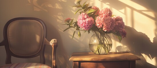 Pretty pink flowers in a glass vase on a wooden table next to a small chair.