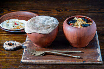 Two clay pots with stewed vegetables on a wooden table, closeup. Stewing food in earthenware is considered healthy - 788711826