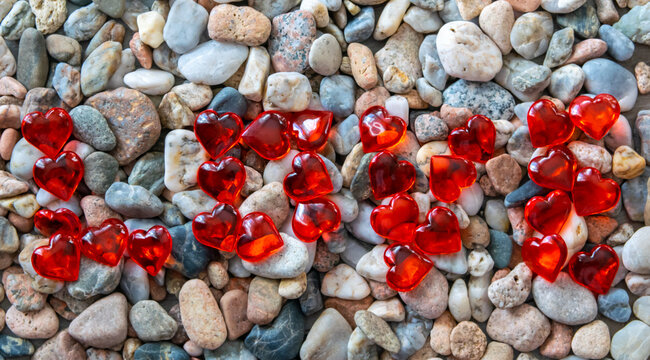 Much red glass hearts on the river pebble stones.