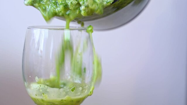 Close-up of glass goblet on a gray background pouring from a blender a healthy smoothie of green vegetables with pieces of cucumber, celery pulp Diet, detox, healing of the body, vitamin cocktail