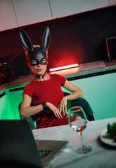 A beautiful girl in a bdsm-style rabbit mask and a bright red dress with leather straps is posing...