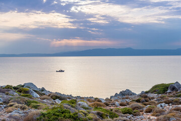 deserted seashore of northern Crete in the light of sunset, fishing boat on the sea, Greece