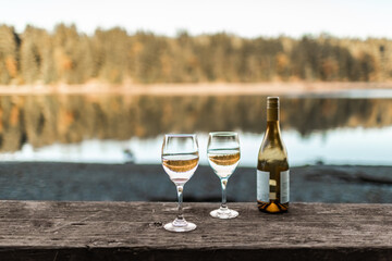 two wine glasses by a peaceful nature lake setting, summer travel concept 