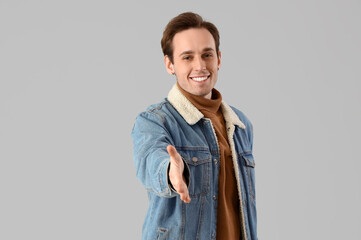 Young man reaching out for handshake on light background - obrazy, fototapety, plakaty