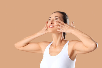 Mature woman giving herself face massage on beige background