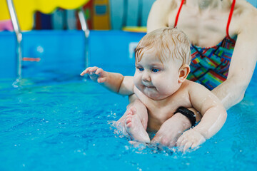 Fototapeta na wymiar A 7-month-old boy is learning to swim in the pool with a coach. Swimming lessons for children. Child development