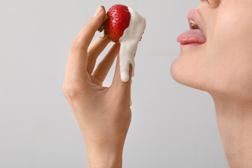 Young woman holding strawberry with white liquid on light background, closeup. Sex concept
