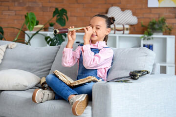 Cute little girl with spyglass and adventure book at home