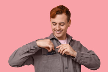 Young man putting credit card into pocket on pink background