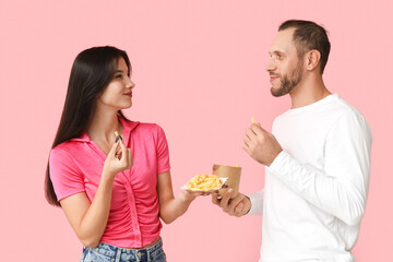Beautiful young couple with french fries on pink background