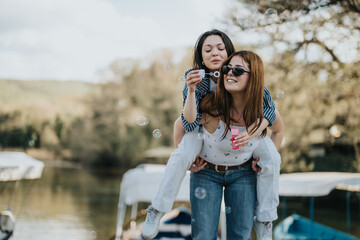 Two young women enjoy a carefree day outdoors, blowing bubbles and laughing by the river, embodying...