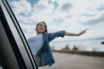 Capture of a joyful young woman, stretching her arm out of a car window, feeling free on a scenic drive along the coast.