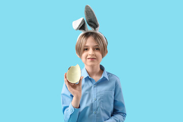 Cute little boy in bunny ears with chocolate egg on blue background. Easter celebration