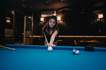 A young woman lines up a shot in a friendly game of pool, exhibiting concentration and enjoyment in...