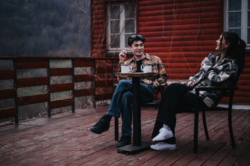 A couple sits in tranquility, sipping coffee together on a homey wooden deck, surrounded by a serene nature backdrop.
