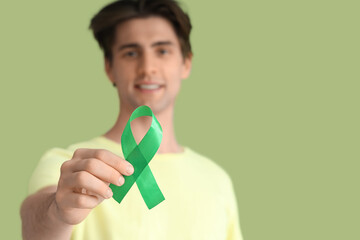 Young man with green ribbon on color background, closeup. Glaucoma awareness month