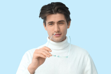 Young man with eyeglasses squinting on blue background, closeup. Glaucoma awareness month