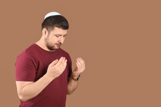 Young Jewish man in hat praying on brown background