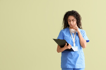 Thoughtful female African-American medical intern with clipboard on green background