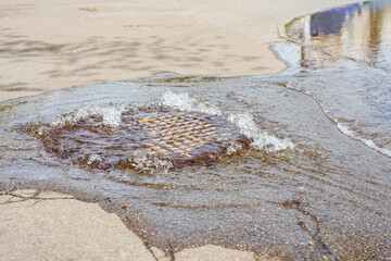 Water fountain pours out from sewer hatch, breakthrough sewerage system. Accident of water supply,...